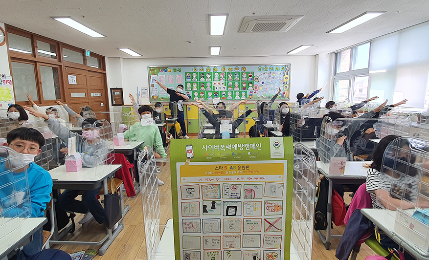 장재초등학교 6학년 5반 친구들이 교실 각자 자리에 앉아 양 손을 뻗으며 사이버폭력예방을 표현한 사진